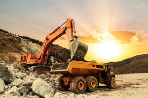 Excavator loading dumper truck on mining site at sunset.